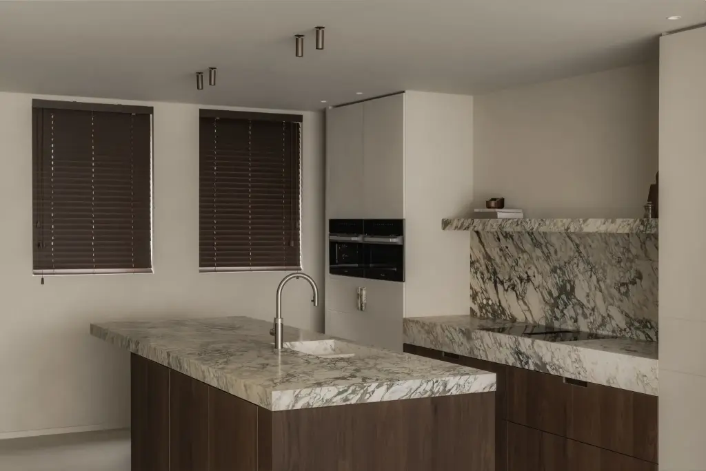 Keuken met kookeiland in natuursteen op een donkere houten onderkast, met ramen met houten jaloezieën, Het Zoute Schorre, interieur Laura Calleeuw