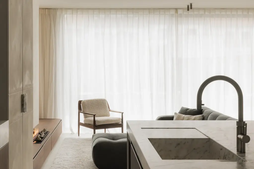 Kookeiland met kraan en een zithoek met fauteuil, sofa en lange vitrage, Het Zoute Schorre, interieur Laura Calleeuw
