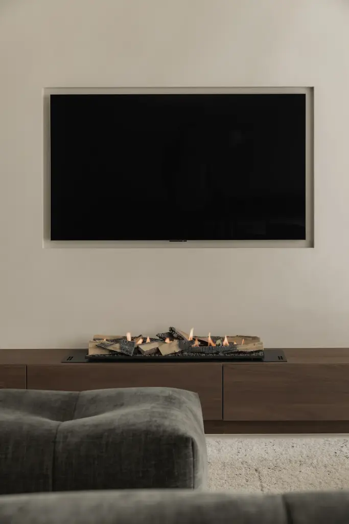 Televisie en laag houten meubel met schaal, met een sofa op de voorgrond, Het Zoute Schorre, interieur Laura Calleeuw