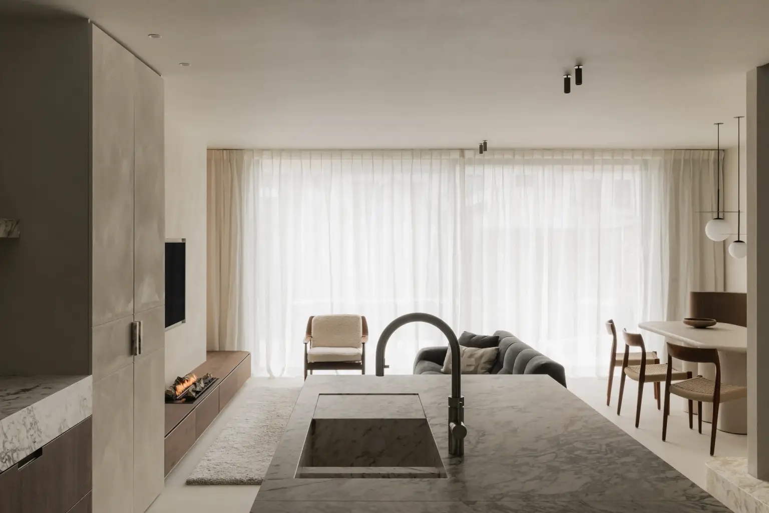 Open leefruimte met kookeiland op de voorgrond, een zithoek met fauteuil en haard en een eethoek achteraan, Het Zoute Schorre, interieur Laura Calleeuw