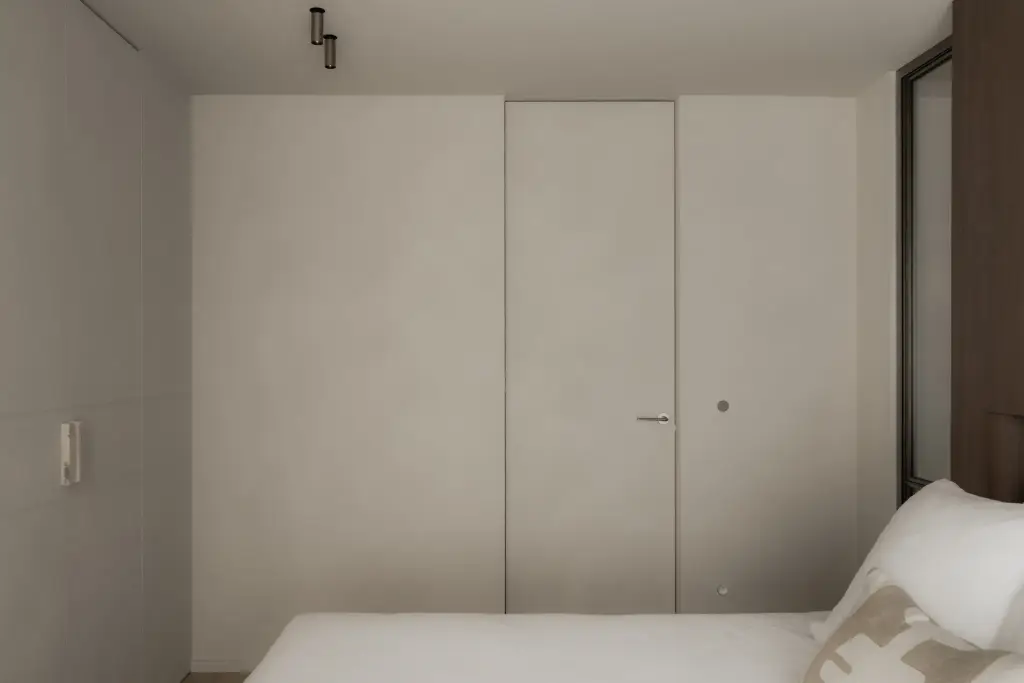 Slaapkamer met vlakke deuren, kastdeuren en de hoek van het bed met kussens, Het Zoute Schorre, interieur Laura Calleeuw
