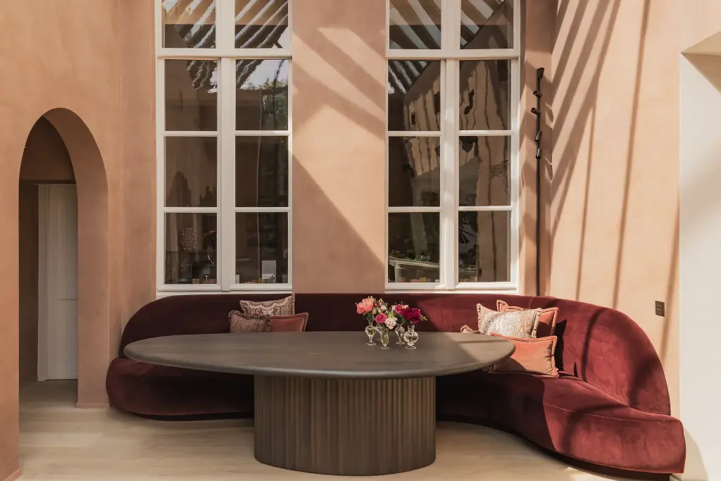 Eethoek met rode fluwelen zitbank, ovale tafel en hoge boogramen, Herenhuis in Brugge, interieur Laura Calleeuw