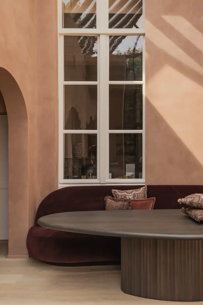 Eethoek met rode fluwelen zitbank, ovale tafel en hoge boogramen, Herenhuis in Brugge, interieur Laura Calleeuw