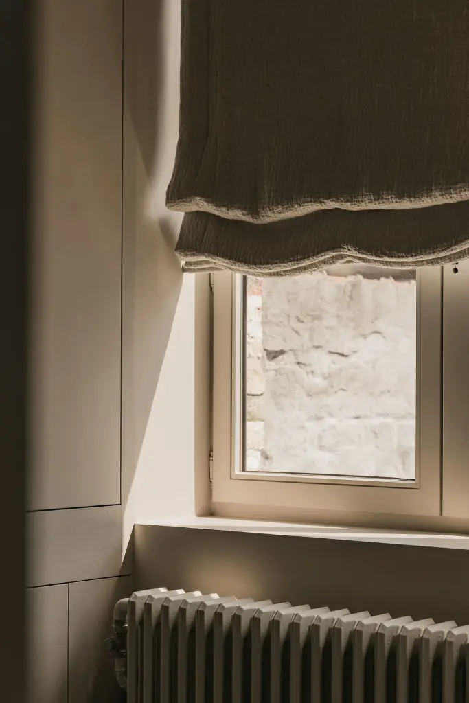 Linnen rolgordijn met golvende rand voor het raam en radiator, Herenhuis in Brugge, interieur Laura Calleeuw