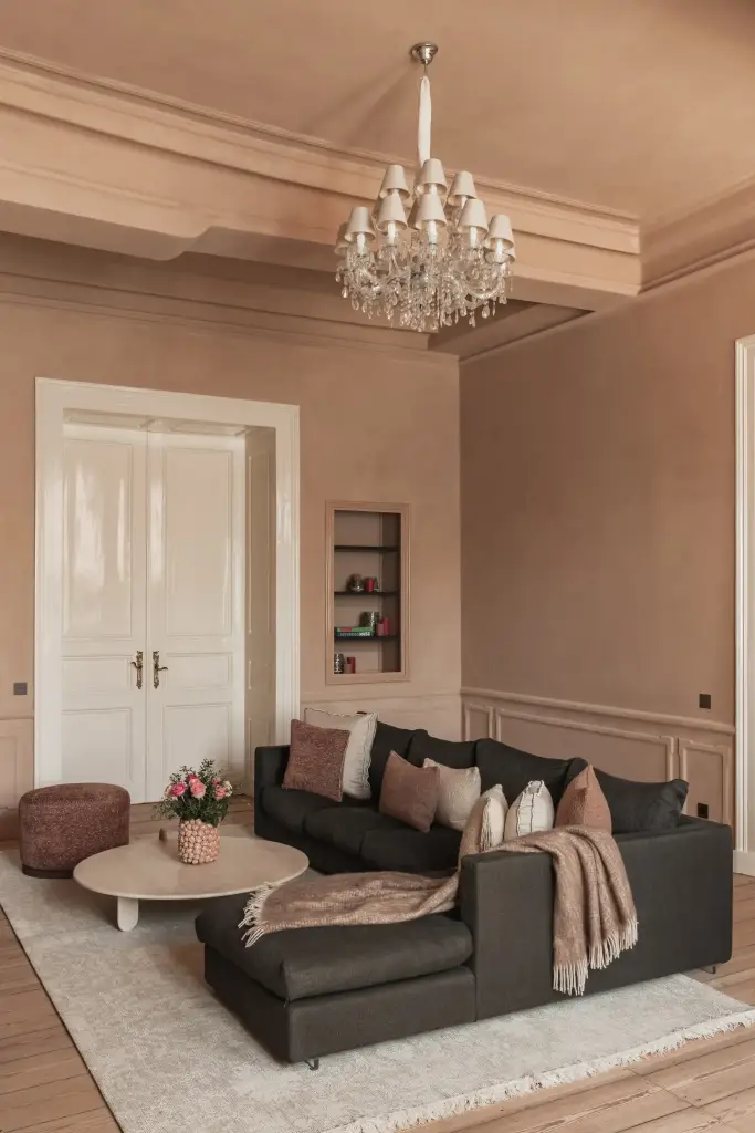 Salon met antracieten hoekzetel, marmeren schouw en kroonluchter in roze kalkverf, Herenhuis in Brugge, interieur Laura Calleeuw