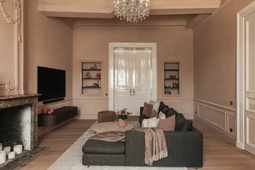 Salon met antracieten hoekzetel, marmeren schouw en kroonluchter in roze kalkverf, Herenhuis in Brugge, interieur Laura Calleeuw