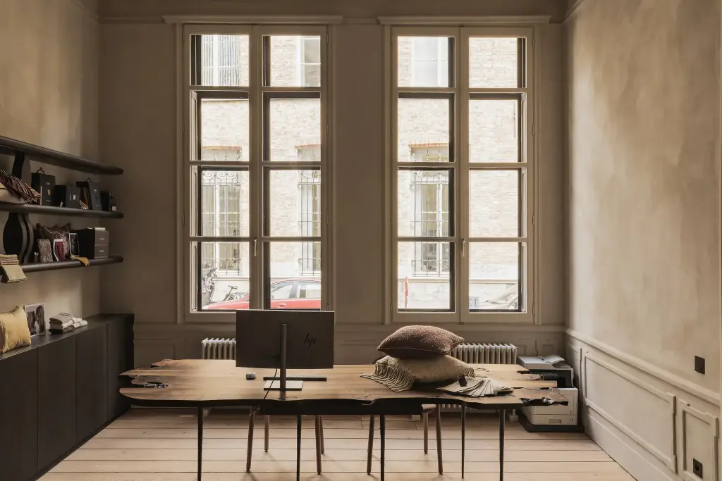 Ruimte met hoge ramen, houten werktafel en stalen op kledingrek, Herenhuis in Brugge, interieur Laura Calleeuw