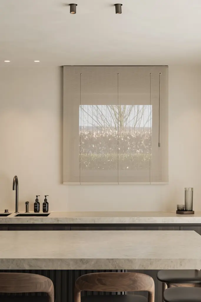 Keukeneiland met barkrukken voor het raam met rolgordijn, Villa in Loppem, interieur Laura Calleeuw