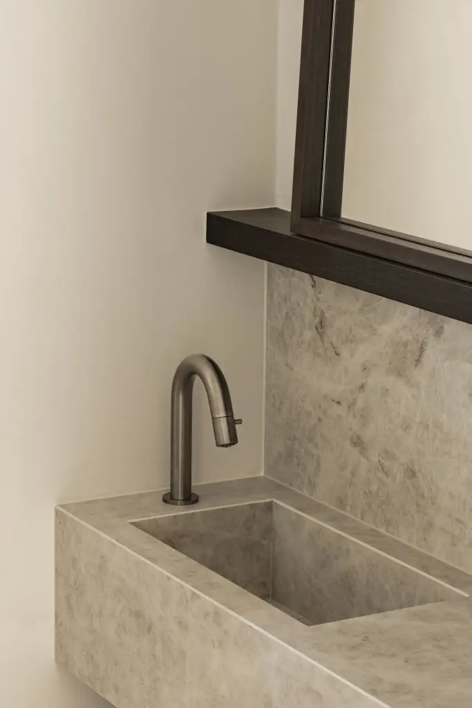 Wastafel in natuursteen met kraan en spiegel in donkere lijst, Villa in Loppem, interieur Laura Calleeuw