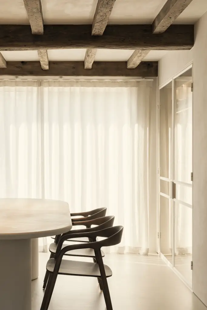Ovale eettafel met houten stoelen voor linnen gordijnen onder een balkenplafond, Totaalrenovatie in Loppem, interieur Laura Calleeuw