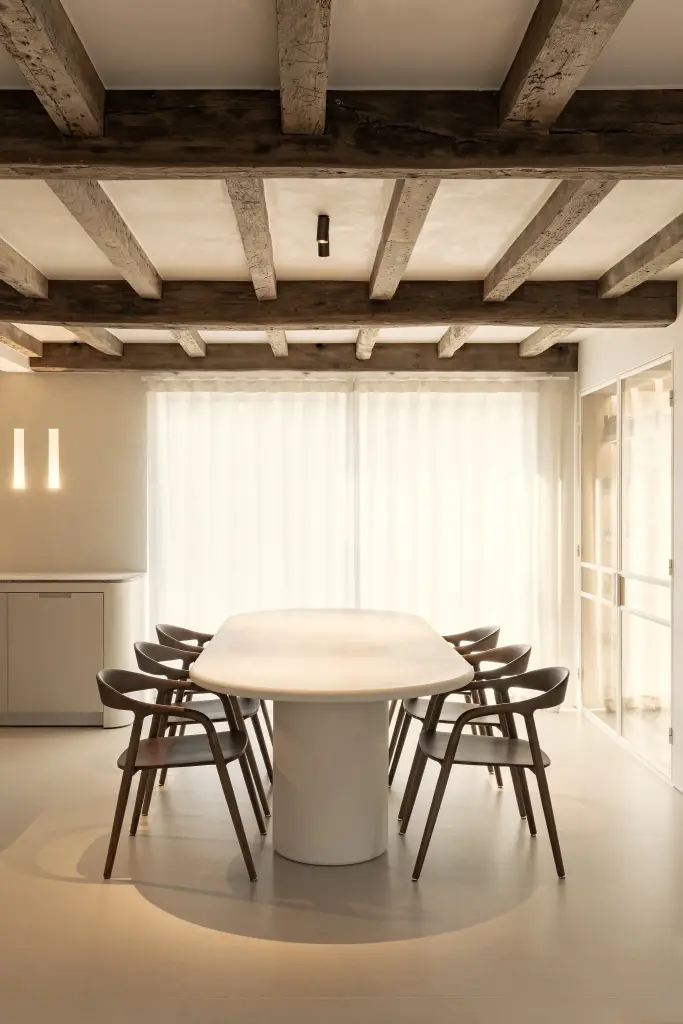 Ovale eettafel met houten stoelen voor linnen gordijnen onder een balkenplafond, Totaalrenovatie in Loppem, interieur Laura Calleeuw