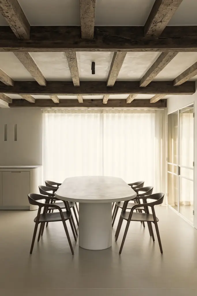 Ovale eettafel met houten stoelen voor linnen gordijnen onder een balkenplafond, Totaalrenovatie in Loppem, interieur Laura Calleeuw