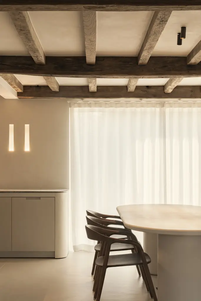 Ovale eettafel met houten stoelen voor linnen gordijnen onder een balkenplafond, Totaalrenovatie in Loppem, interieur Laura Calleeuw