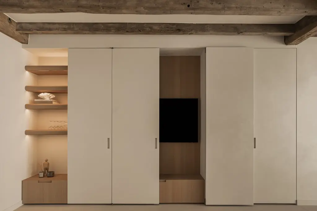 Kastenwand met verdoken televisie in eikenhouten nis en open planken onder een houten balk, Totaalrenovatie in Loppem, interieur Laura Calleeuw