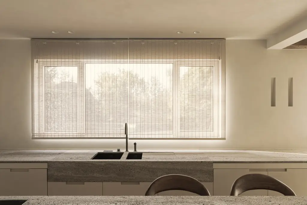 Keuken met spoelbak in travertijn werkblad voor het raam met rolgordijn, Totaalrenovatie in Loppem, interieur Laura Calleeuw
