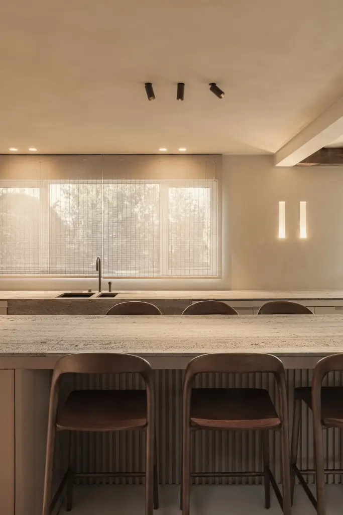 Keukeneiland met barkrukken en spots voor het raam met bamboe rolgordijn, Totaalrenovatie in Loppem, interieur Laura Calleeuw