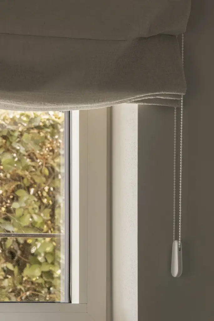 Detail van een linnen rolgordijn voor een raam met uitzicht op de tuin, Totaalrenovatie in Loppem, interieur Laura Calleeuw