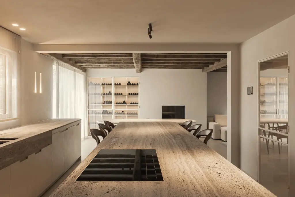 Lang travertijn eiland met kookplaat met zicht op eethoek en wijnkast, Totaalrenovatie in Loppem, interieur Laura Calleeuw