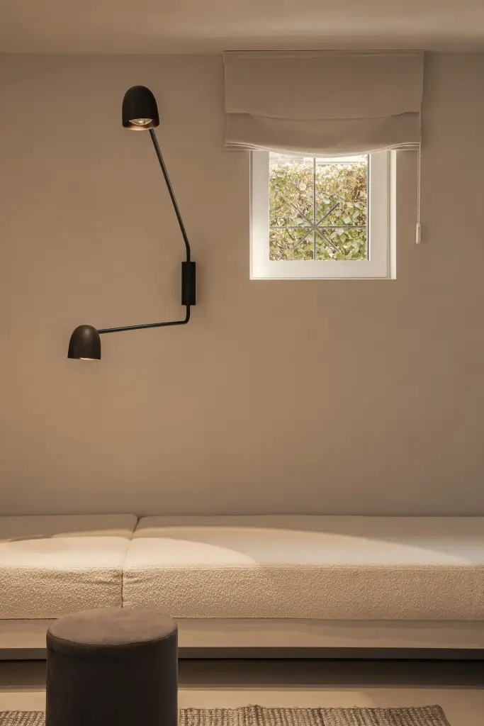 Zithoek met crème bank, poef, zwarte wandlamp en klein raam, Totaalrenovatie in Loppem, interieur Laura Calleeuw