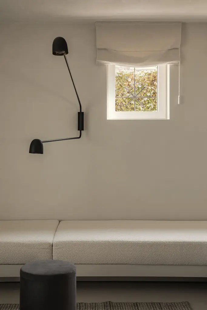 Zithoek met crème bank, poef, zwarte wandlamp en klein raam, Totaalrenovatie in Loppem, interieur Laura Calleeuw