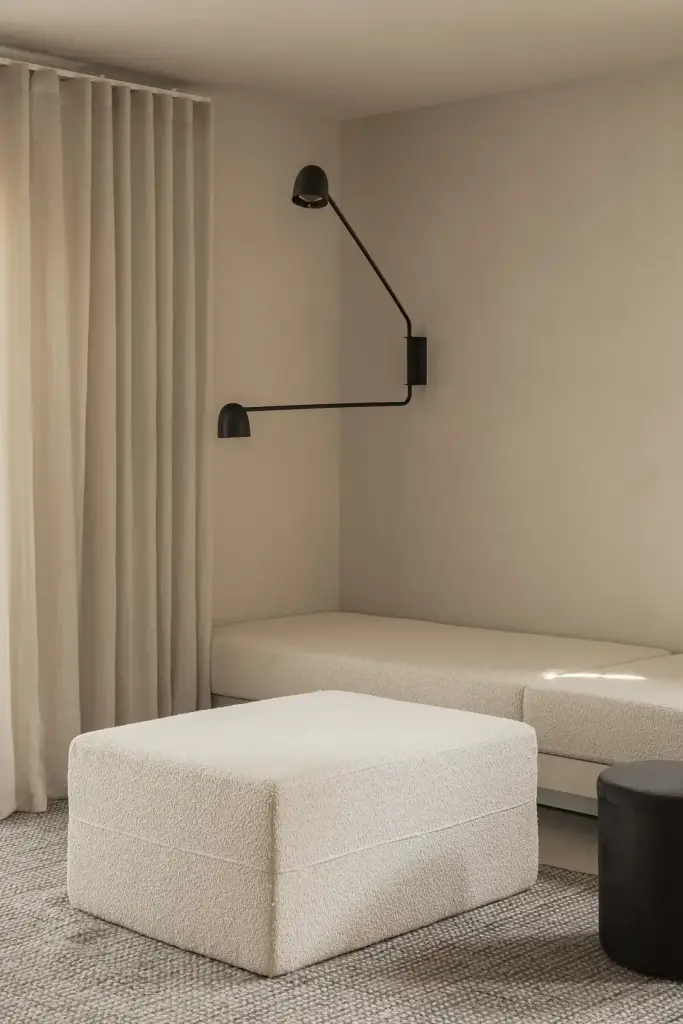 Zithoek met crème bank, poef, zwarte wandlamp en klein raam, Totaalrenovatie in Loppem, interieur Laura Calleeuw