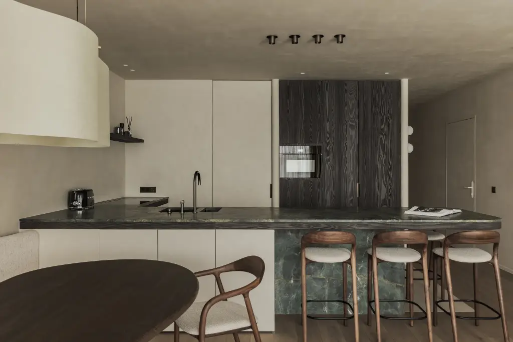 Keuken met eiland in groen marmer, houten barkrukken en ovenkast in donker eiken, Appartement in Knokke, interieur Laura Calleeuw