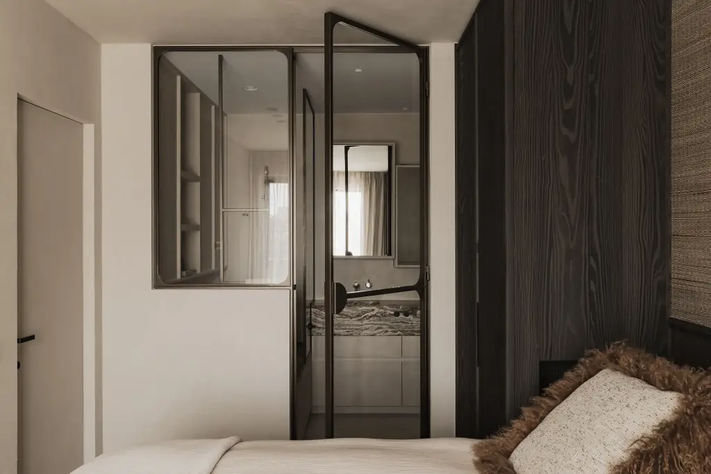 Slaapkamer met stalen glaswand en doorkijk naar de badkamer met onyx wastafel, Appartement in Knokke, interieur Laura Calleeuw