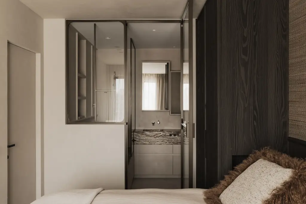 Slaapkamer met stalen glaswand en doorkijk naar de badkamer met onyx wastafel, Appartement in Knokke, interieur Laura Calleeuw