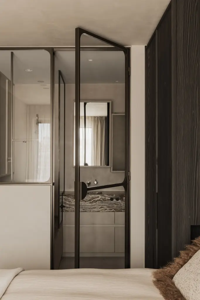 Slaapkamer met stalen glaswand en doorkijk naar de badkamer met onyx wastafel, Appartement in Knokke, interieur Laura Calleeuw