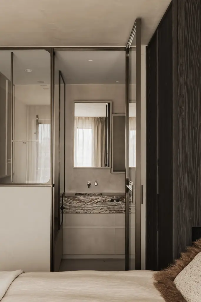 Slaapkamer met stalen glaswand en doorkijk naar de badkamer met onyx wastafel, Appartement in Knokke, interieur Laura Calleeuw