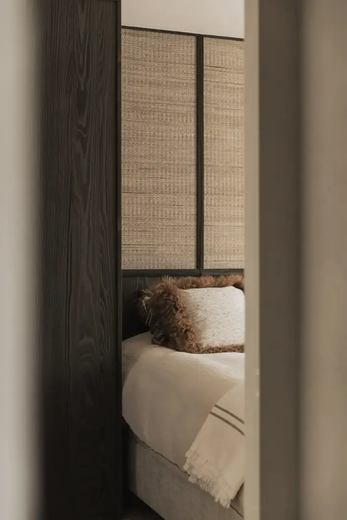 Slaapkamer met rieten wandbekleding, donker hout en vachtkussen op het bed, Appartement in Knokke, interieur Laura Calleeuw