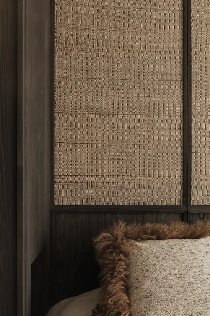 Slaapkamer met rieten wandbekleding, donker hout en vachtkussen op het bed, Appartement in Knokke, interieur Laura Calleeuw