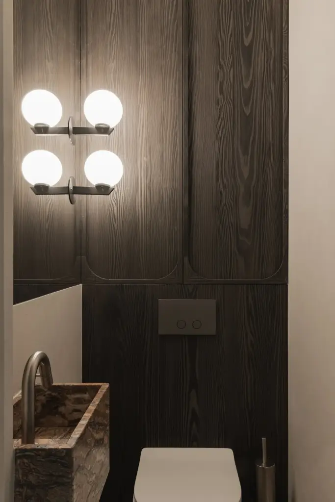 Toilet met vier bolvormige lampen, donker eiken kastenwand en onyx fonteintje, Appartement in Knokke, interieur Laura Calleeuw