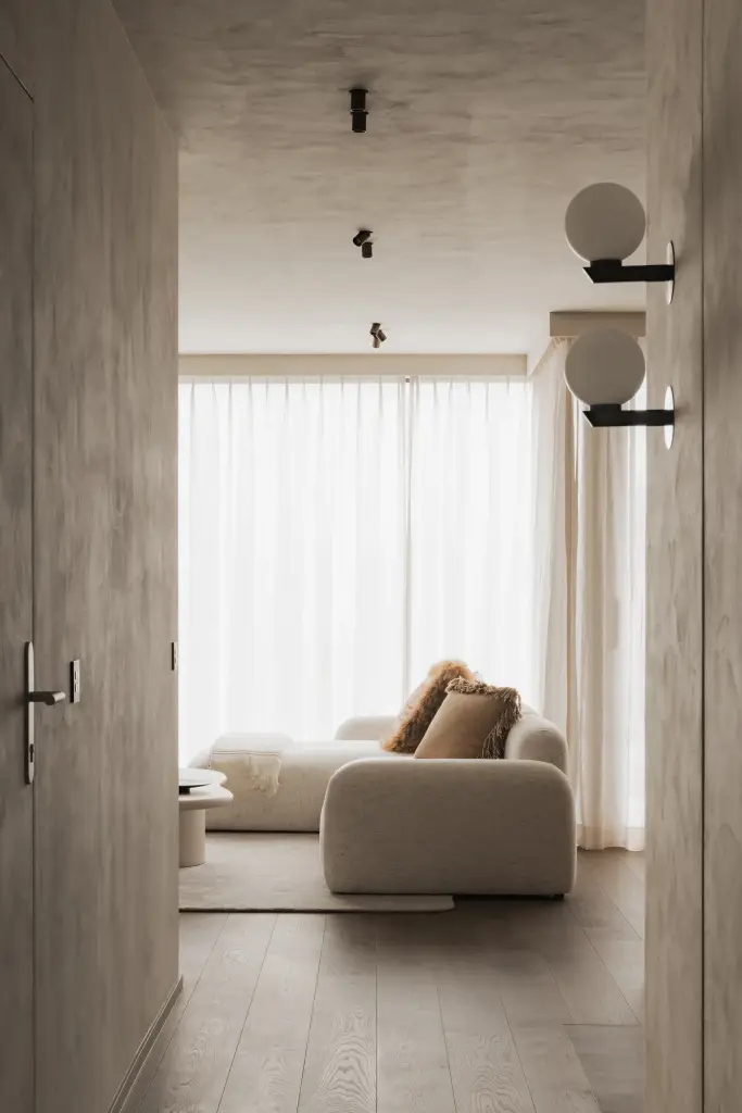 Doorkijk naar de woonkamer met bolvormige wandlampen, zetel en eettafel, Appartement in Knokke, interieur Laura Calleeuw