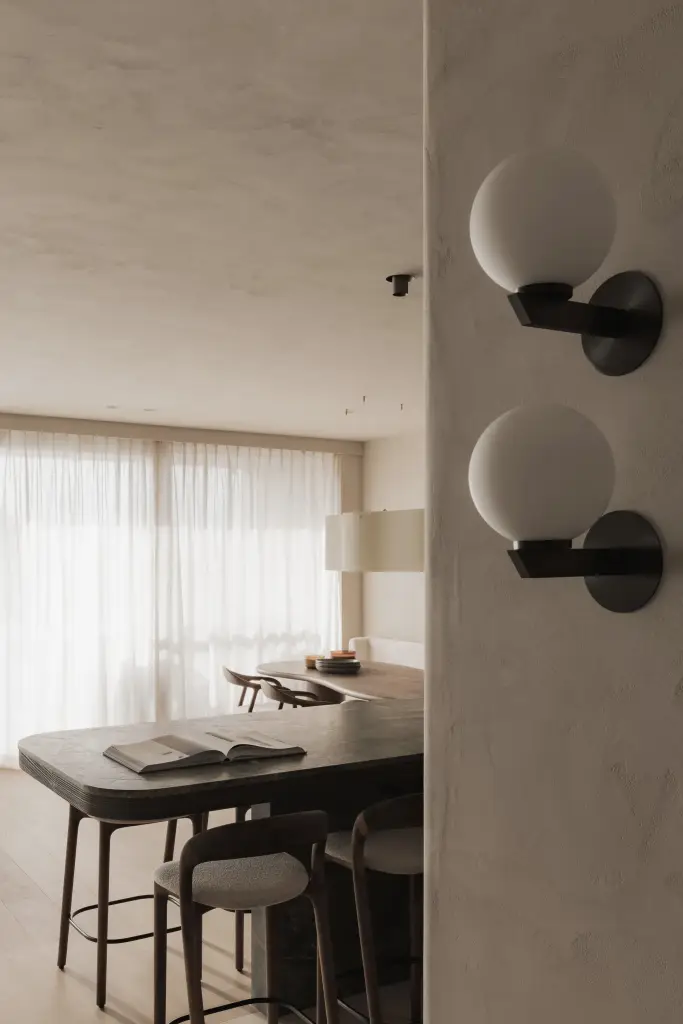 Doorkijk naar de woonkamer met bolvormige wandlampen, zetel en eettafel, Appartement in Knokke, interieur Laura Calleeuw