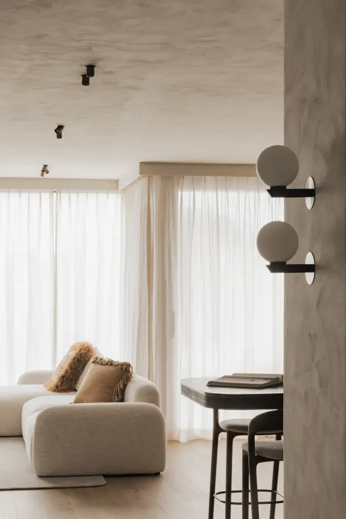 Doorkijk naar de woonkamer met bolvormige wandlampen, zetel en eettafel, Appartement in Knokke, interieur Laura Calleeuw
